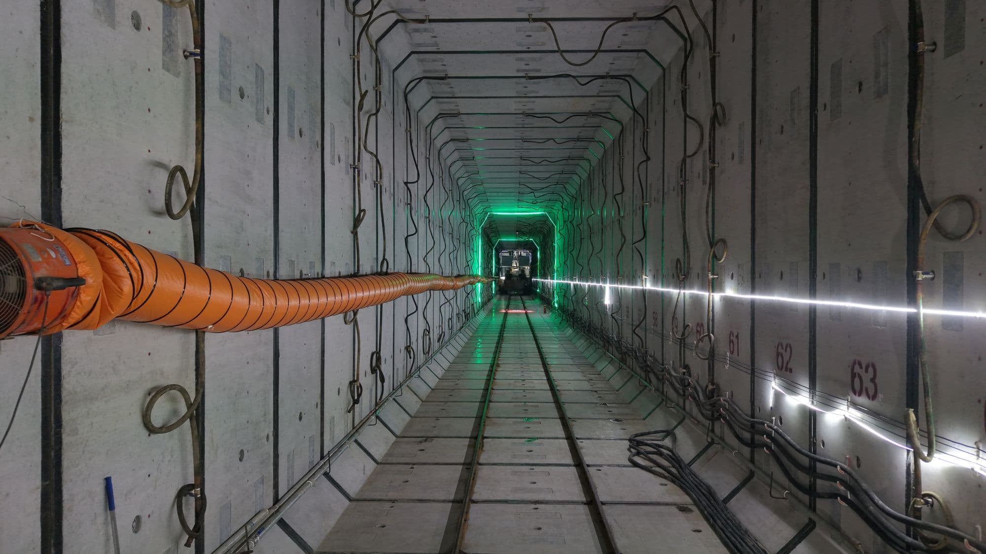 Interior view of a rectangular tunnel during construction, with temporary ventilation and utility systems